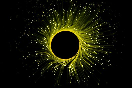 Many illuminated yellow fiber optic light strands in ring formation against black background