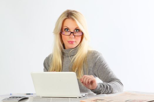 The business woman wearing spectacles with newspapers and the laptop works behind a table