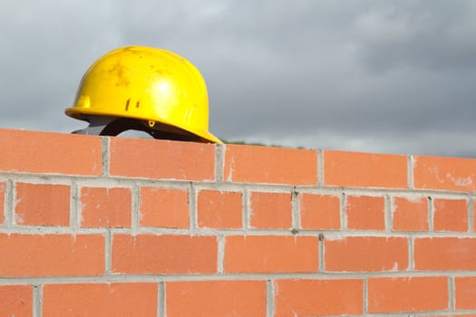 A yellow safety helmet on the top of a red brick wall with pointing.