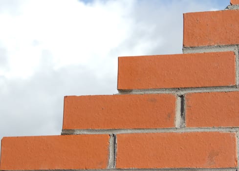 Red bricks constructed into a wall with cement pointing and a stepped jagged edge against a cloudy sky.