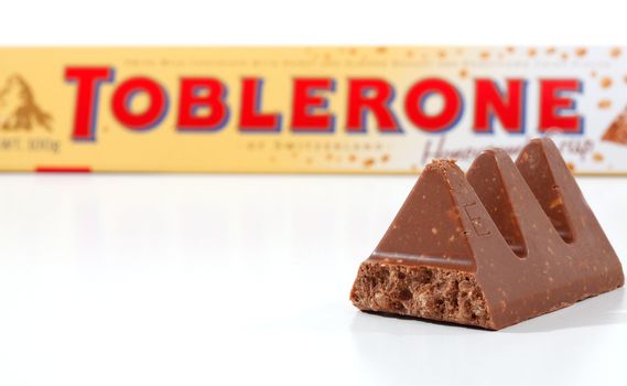 Toblerone chocolate containing honey and almond nougat and crispy rice pieces. Toblerone packaging in background  Toblerone is made in Switzerland by Kraft Foods.  Focus to foreground pieces.  