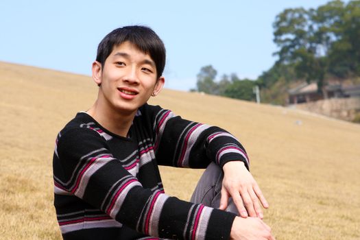 handsome forties man is sitting on the grass relaxing and smiling. 