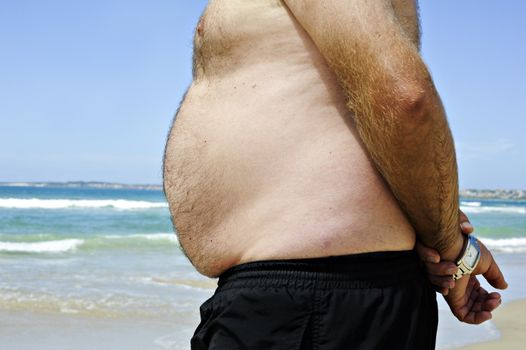 Fat man on the beach showing his unhealthy belly