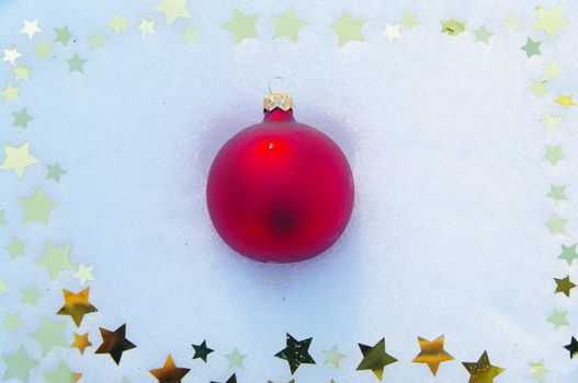 red bauble and golden snow stars on a real snowy icy surface