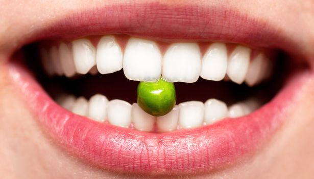 Female smile with pea between teeh in a mouth. Diet concept.