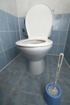 white clean toilet, wc brush in foreground, tiled floor and walls, blue color
