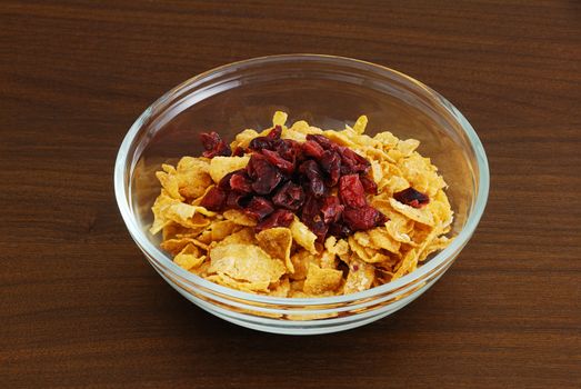 Cornflakes with dried cranberries in glass bowl on dark wooden table