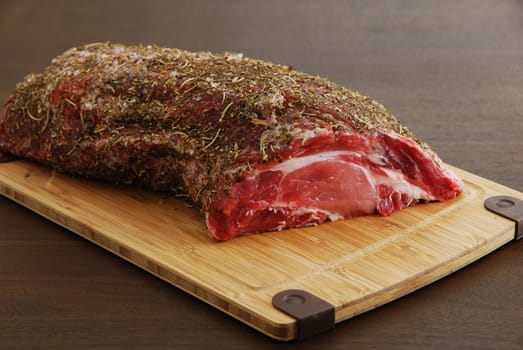 Raw  meat with spices ready for cooking and lying on bamboo board over dark wooden table