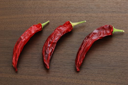 Three dried hot red chili peppers lying on dark wooden table