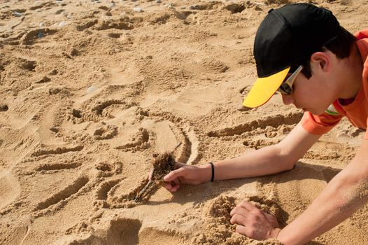 Creative teenager sketching a cartoon on beach sand