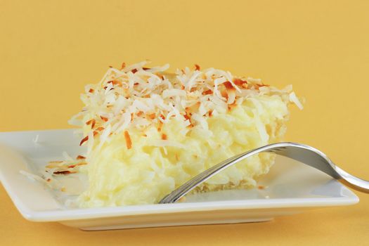 Slice of homemade coconut cream pie against a yellow background.
