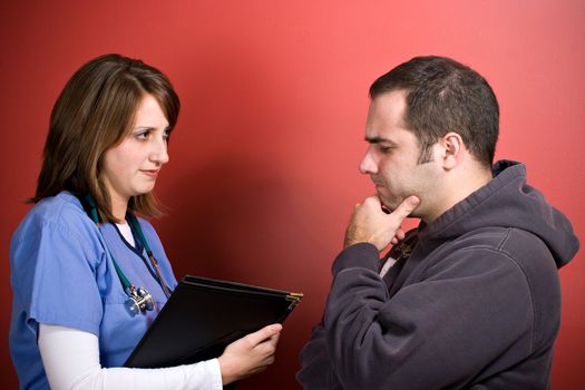 A young nurse talks to a patient during his visit. The man looks concerned about his health.