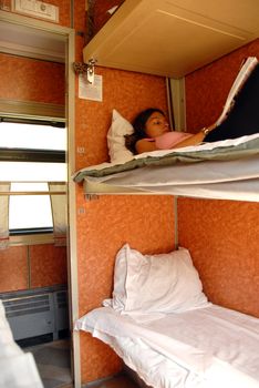 girl lying and reading a book in sleeping wagon in train
