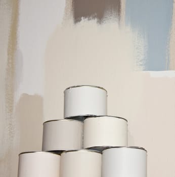 Stack of paint boxes with different shades of white, against a wall covered in paint samples