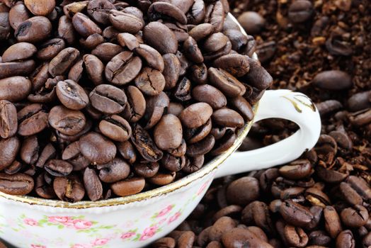 Cup filled with coffee beans over a background of whole and freshly ground coffee beans. Extreme shallow depth of field with selective focus on beans in cup.