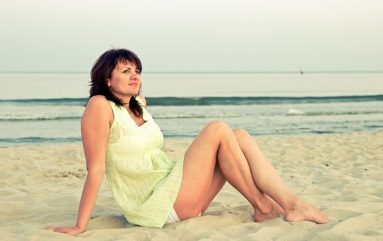 The woman sits on a beach in the evening
