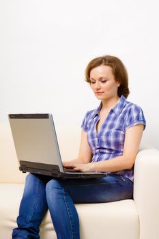 Young attractive girl with a laptop sitting on the sofa at home