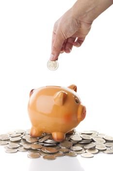 Female hand inserting a two Euros coin on a Piggy bank isolated over a white background