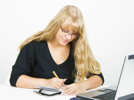 blonde girl with a laptop writes in a notebook