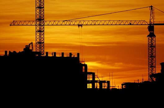 construction of a building, cranes and other machinery as silhouettes against a background of red sunset sky