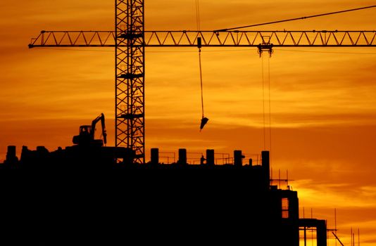 construction of a building, cranes and other machinery as silhouettes against a background of red sunset sky