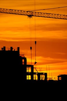 construction of a building, cranes and other machinery as silhouettes against a background of red sunset sky