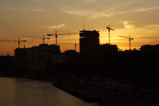 construction of a building, cranes and other machinery as silhouettes against a background of red sunset sky