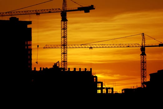 construction of a building, cranes and other machinery as silhouettes against a background of red sunset sky