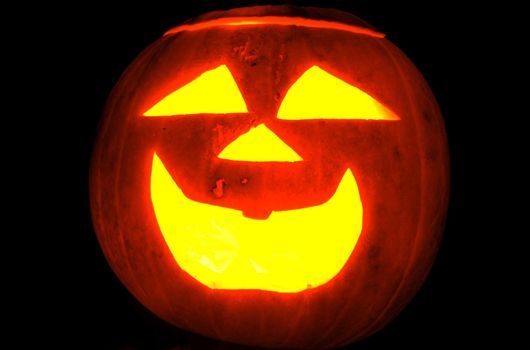 A traditional jack-o-lantern pumpkin carved into a smiley face. Orange and yellow isolated on #000000 black.