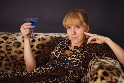 Girl in leopard dress, drinking a cocktail on sofa