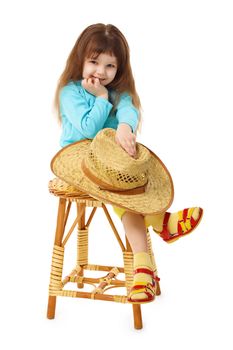 The child sits on an old wooden chair with a straw hat in hand isolated on white background