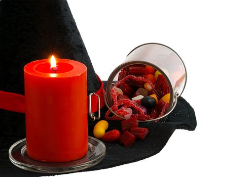 Halloween candies and burning orange candle on edge of witch hat isolated on white background
