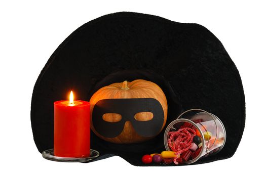 Halloween candies, burning orange candle and masqueraded pumpkin inside black witch hat isolated on white background
