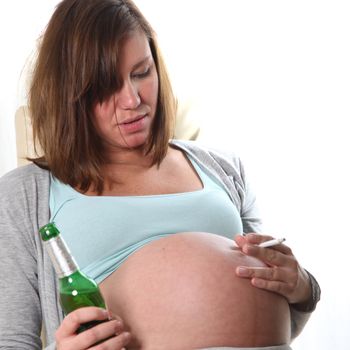 a pregnant woman sitting drunk on a chair holding a cigarette in front of her belly. In her right hand she holds a bottle of beer.
