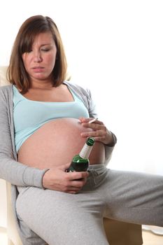 pregnant women smoke and drink alcohol. She holds a bottle of beer and a cigarette in the hand and is drunk
