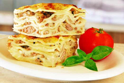 two appetizing lasagna pieces with basil and tomato on white plate