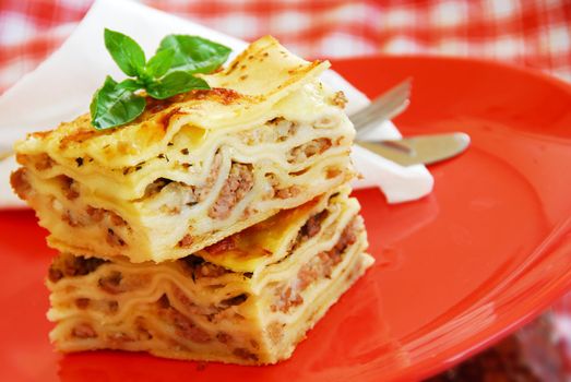 appetizing lasagna piece with basil on red plate