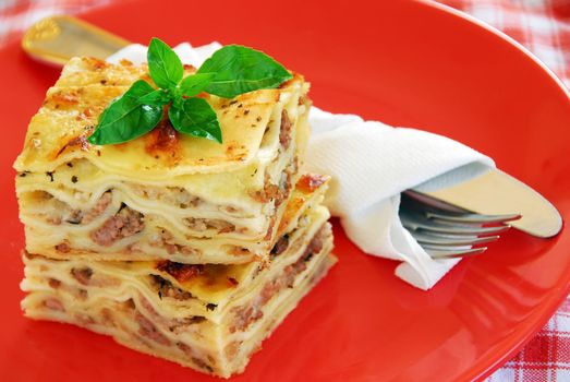 appetizing lasagna piece with basil on red plate