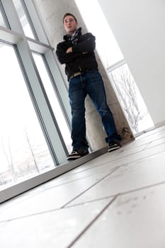 A young man standing by some large windows from a low angle perspective.