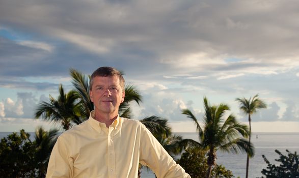 Retired man smiling as the sun sets behind over the palm lined ocean