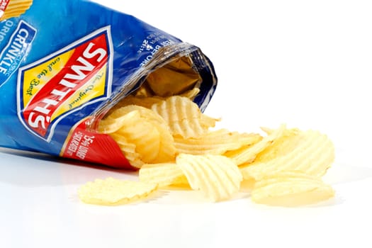 An opened 45g packet of Smith's Potato crinkle cut chips with the crisps spilling out of the packet.  Smith's chips are owned by PepsiCo.  Photographed on a white background.  Editorial Use Only.  