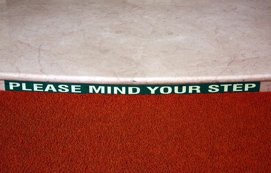 A 'Mind Your Step' sign on a marble step.