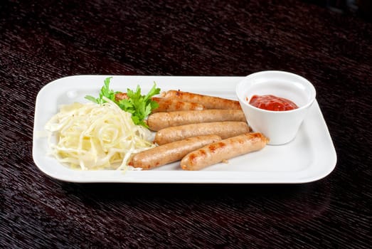 Grilled sausages with cabbage, greens and tomato sauce on white plate