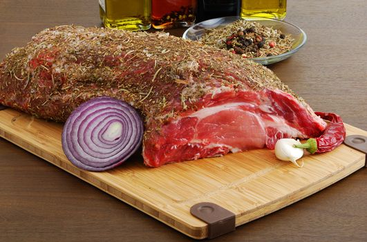 Raw  meat with spices ready for cooking and lying on bamboo board over dark wooden table and flavored olive oil at background