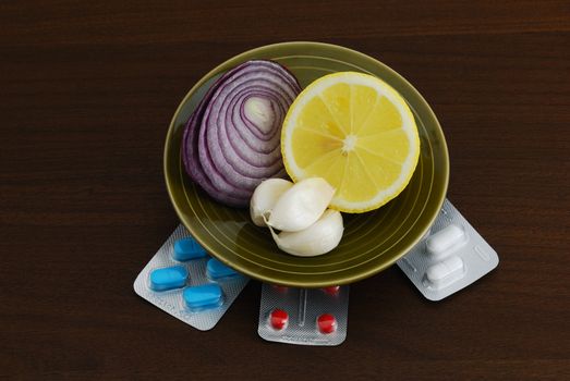 Set of alternative remedies for flu treatment including lemon, garlic and onion standing on set of pills on dark wooden table