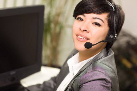 Attractive Young Mixed Race Woman Smiles Wearing Headset Near Her Computer In An Office Setting.