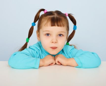 Little girl sitting at a desk on blue background