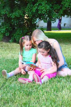 Young mum reads to the children the book during walk in park