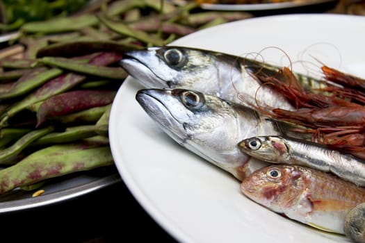 Fresh fish and prawns on plate with beans in background