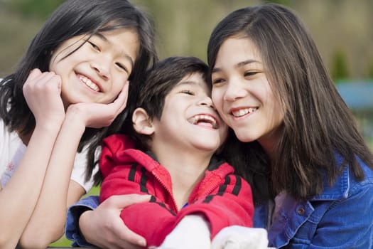 Two sisters and their disabled little brother sitting together at the park, biracial part Thai- Scandinavian descent.